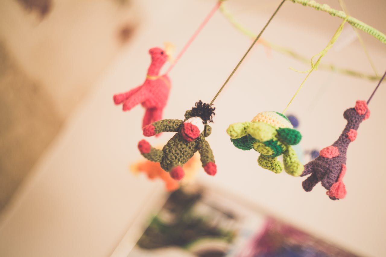 our-story Colorful knitted animal toys hanging from a nursery mobile creating a playful atmosphere.
